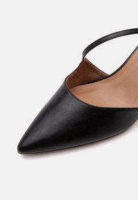 Chaussure slingback en cuir noir à bout pointu avec une semelle intérieure beige et une fine bride autour du talon.