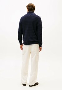 Pullover in maglia blu navy con colletto alto, caratterizzato da un motivo a strisce testurizzato. Abbinato a pantaloni a gamba larga crema con tasche laterali.
