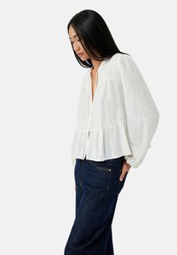 Witte, loszittende blouse met een peplumrand, gestructureerde stof, knoopsluiting en lange, ballonmouwen, gecombineerd met donkerblauwe denim broek.