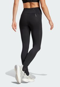 Black athletic leggings with high waist, textured fabric, and side pocket detail, paired with light gray running shoes.