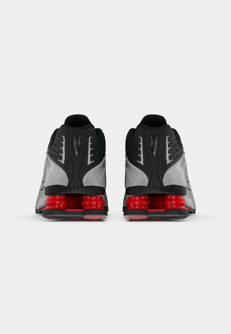 Une paire de chaussures de sport noires et grises avec des talons rouges en forme de ressort, faisant face vers l'avant sur un fond blanc.