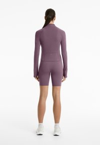 Lila enganliegendes Langarmoberteil und passende Shorts aus dehnbarem Stoff, mit hohem Kragen, nahtlosem Design und schlanker Silhouette.