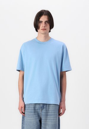 Tricou din bumbac de culoare albastră deschisă, cu guler rotund și mâneci scurte, având o croială lejeră și o textură netedă și moale.