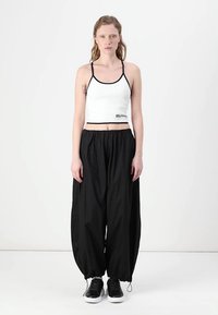 Hvit kort tank topp med svart kant, kombinert med løse svarte bukser. Skoene er svarte med hvite såler. Enkelt design, ingen mønstre.