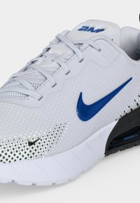 Λευκό παπούτσι τρεξίματος Nike Air Max με μπλε λογότυπο Swoosh, λευκά κορδόνια, και ορατή αερόσολα στην σόλα.