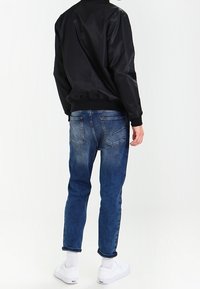 Svart, lätt bomberjacka med ribbade muddar, i kombination med blekta blå denimjeans och vita sneakers. Rent snitt och avslappnad passform.