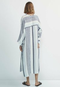 Robe longue et ample à rayures horizontales blanches et bleues marine, en tissu texturé. Comprend des manches larges et des fentes latérales.