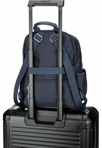 Zaino navy con texture a rete fissato su una valigia rigida nera. Presenta spallacci regolabili e una maniglia superiore.