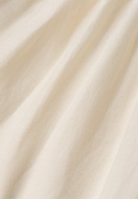 Tela de lino color crema, texturizada con un sutil tejido. Pliegues suaves crean sombras delicadas, destacando sus cualidades ligeras y transpirables.