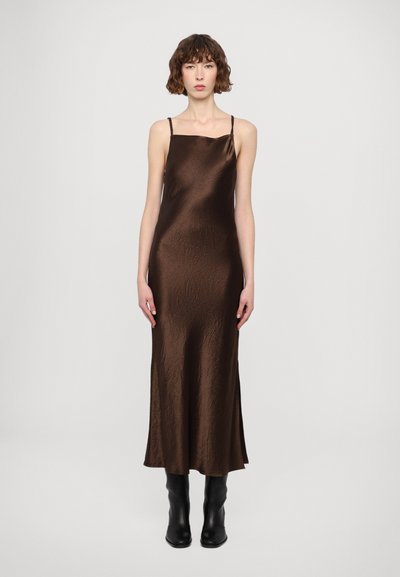 Une robe nuisette marron en satin avec une texture légèrement froissée, un décolleté carré et des fines bretelles. Associée à des bottes noires à talons jusqu'aux genoux.