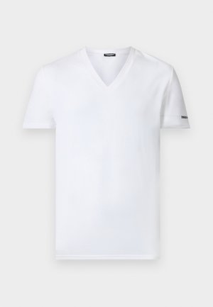 Άνδρας στέκεται ξυπόλητος, φοράει λευκό T-shirt με V-λαιμόκοψη και μαύρα boxer, κοιτώντας προς τα πλάγια σε απλό λευκό φόντο.