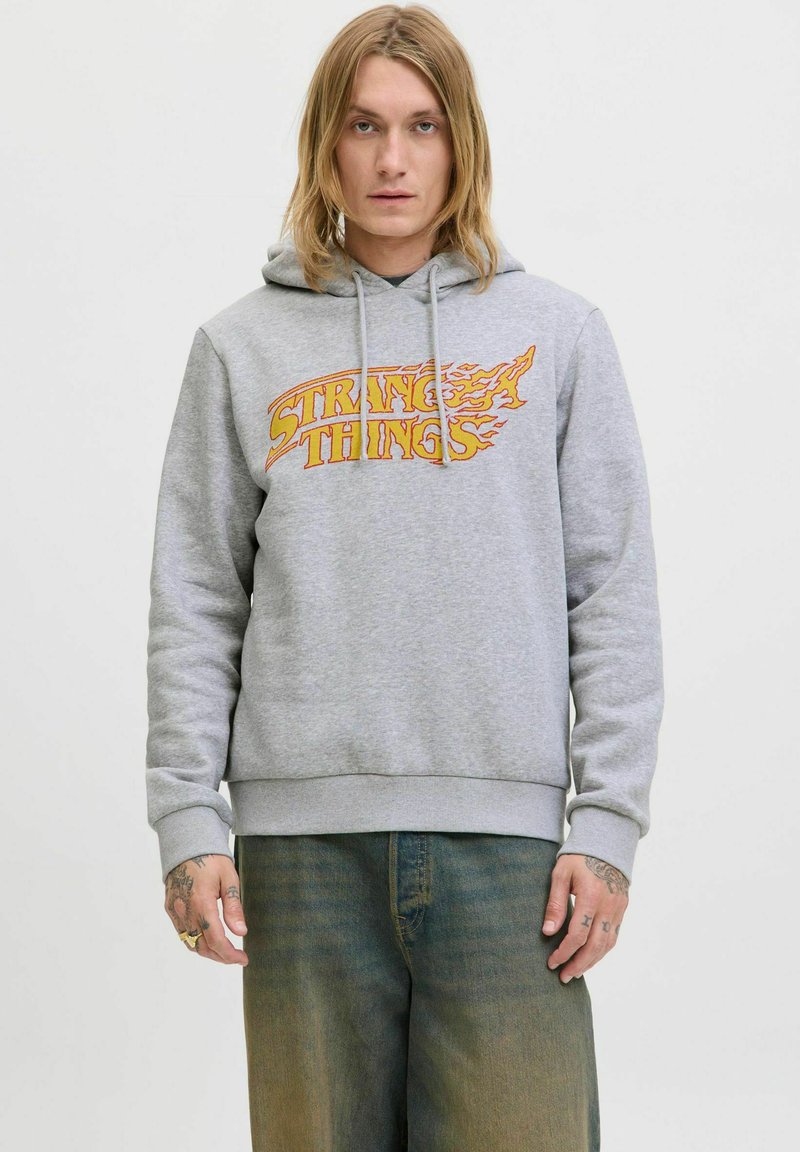 Haut à capuche gris en tissu doux. Présente un graphique sur le devant avec la mention "STRANGE THINGS" en orange avec des accents de flammes. Poche kangourou incluse.