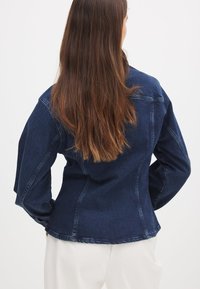 Denim jacket in dark blue, featuring a classic design, long sleeves, and a structured fit with visible seams and back yoke detail.