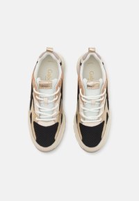 Beige och svarta sneakers med mesh- och mocka-paneler, vita snören och en gyllene detalj vid hälen. Tjocka, vadderade sulor för komfort.