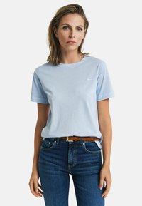 Lyseblå bomulds T-shirt med rund hals og korte ærmer, der har en lille logo-detalje på venstre bryst. Bæres med mørkeblå jeans.