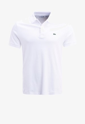 Biała koszulka polo wykonana z bawełny; posiada kołnierzyk, krótki rękaw oraz małe zielone logo krokodyla na lewej piersi. Prosty design.