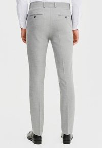 Szare, dopasowane spodnie z teksturowanym wykończeniem, charakteryzujące się wąskim krojem, dwiema tylnymi kieszeniami i czarnymi guzikami. Noszone z wypolerowanymi czarnymi butami.