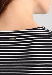 Haut rayé noir et blanc avec un large décolleté, doté d'une petite étiquette métallique à l'arrière. Texture douce, coupe ajustée.