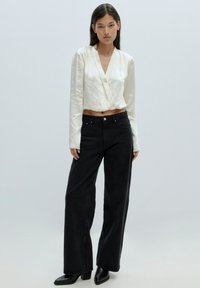 Witte gekruiste cropped top met lange mouwen, gedragen met zwarte wide-leg jeans en zwarte chunky haklaarzen. Glad materiaal en gestructureerde pasvorm.