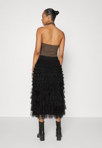 Black tiered tulle skirt with ruffled texture and elastic waistband, paired with a brown strapless top. Model wears black heeled boots.
