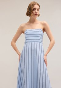 Rochie fără bretele dintr-un material bleu deschis cu dungi verticale bleumarin, având un corset ajustat și o fustă în linie A fluidă. Textură netedă.