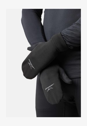 Muffole nere Swedemount indossate sopra una maglia a maniche lunghe nera, mani incrociate davanti al corpo su sfondo chiaro.