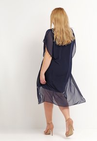 Robe transparente bleu marine avec des manches courtes, design ample et une jupe fluide qui tombe jusqu'au mollet, associée à des escarpins nude.