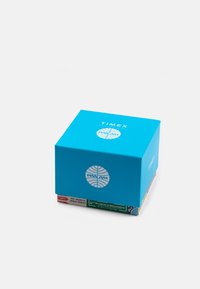 Caixa quadrada turquesa com o texto branco "TIMEX" e logótipos "PAN AM". A base apresenta gráficos temáticos de companhias aéreas multicoloridos. Acabamento suave.