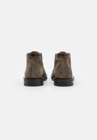 Bruna mockaskinnankelboots med en slät läderdetalj, rund tå och en robust, mörk träsoffa; synlig sömspecifikation vid hälen.