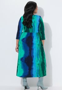 Lang kjole med blå og grøn stribet mønster, med en tætsiddende overdel og udvidet nederdel. Materialet ser glat og let ud.