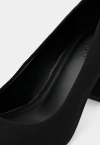 Gros plan de l'intérieur et du talon d'une chaussure à talon haut en daim noir avec un bout arrondi.