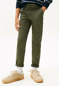 Olivgröna, slim-fit chinos med knappstängning, upprullade muddar och sidofickor, tillsammans med beige mockaskor och vita strumpor.