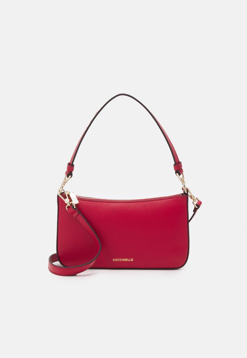 Sac à bandoulière en cuir rouge avec fermeture éclair dorée, bandoulière amovible et logo doré "Coccinelle" sur le devant, sur fond clair uni.
