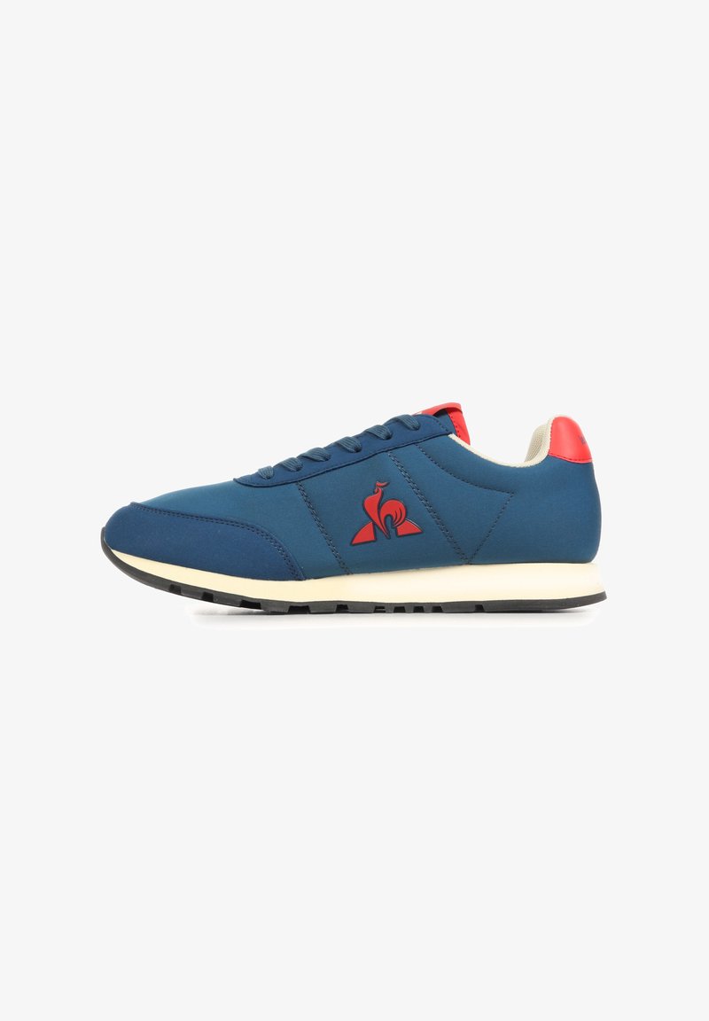 Zapatilla deportiva para hombre en azul marino con lengüeta roja en el talón, logo rojo en el lateral, suela blanca y dibujo de la suela en negro, mostrada de perfil.