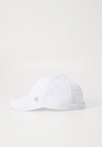 Hvit cap laget av bomull, med buet skjerm, seks-panel design, og brodert "ck" logo i sølv på siden.
