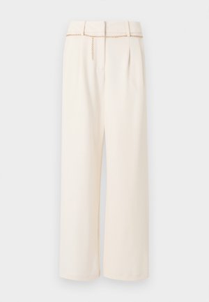 Kremne hlače širokih nogavic z visokim pasom, sprednjimi gubami in tankim zlatim pasom z verižico, položene na ravno svetlo ozadje.