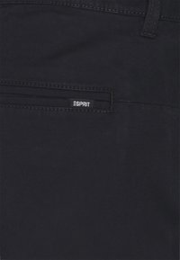 Svarta tygbyxor med en bakficka som har en sömnad logotypetikett. Slät textur och minimalistisk design utan synliga mönster.