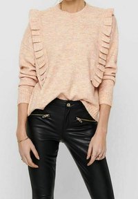 Brzoskwiniowy sweter dziany z marszczeniami na ramionach, w zestawieniu z dopasowanymi czarnymi skórzanymi spodniami z kieszeniami na suwak.