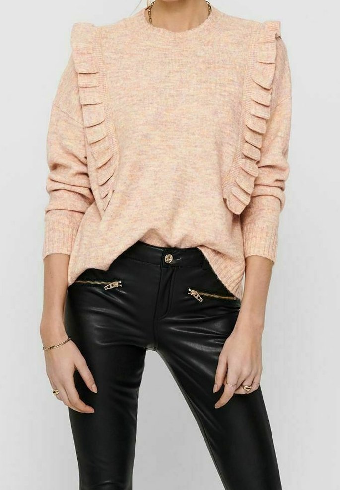 Brzoskwiniowy sweter dziany z marszczeniami na ramionach, w zestawieniu z dopasowanymi czarnymi skórzanymi spodniami z kieszeniami na suwak.