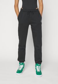 Svarta sweatpants med dragsko i midjan, med sidofickor och en liten logotyp. Bärs med gröna högstövlade sneakers med vita detaljer.