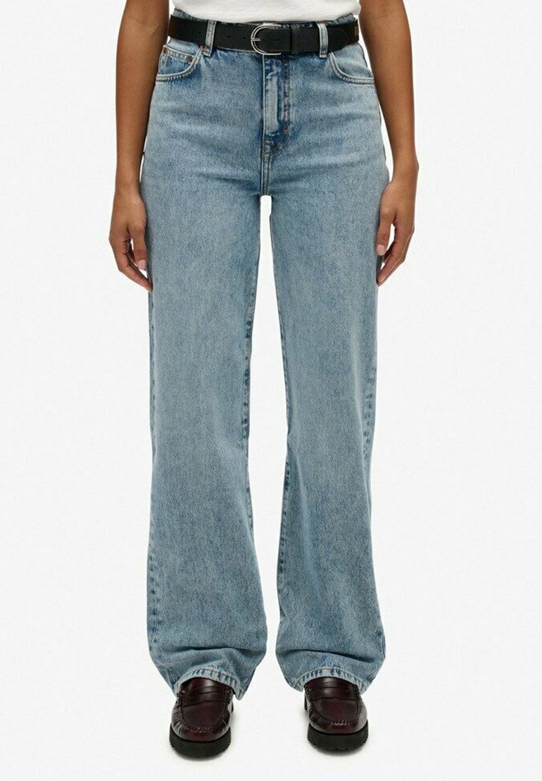 Lichtblauwe denim broek met wijde pijpen en hoge taille. Beschikt over een klassiek vijf-pocket ontwerp en riemlussen, gecombineerd met donkere schoenen.