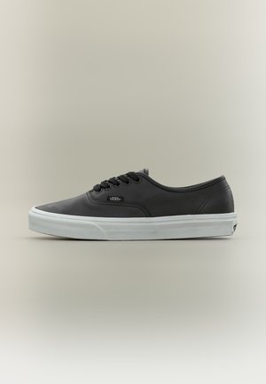 Baskets basses noires Vans avec lacets noirs, semelle en caoutchouc blanche et logo Vans sur le côté et le talon.
