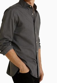 Szara koszula zapinana na guziki, wykonana z miękkiego materiału, z kołnierzem typu spread, długimi rękawami z podwiniętymi mankietami oraz lekko zaokrąglonym dołem.