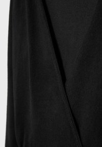 Detailný záber na čiernu tkaninu s viditeľným švom a záhybmi, zdôrazňujúci textúru a šitie odevu.