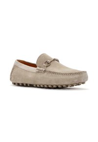 Mocasines de ante en gris claro con punta redonda, correa decorativa de cuero y acento metálico, que cuentan con una suela de goma texturizada.