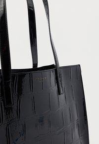 Black patent leather tote bag with a glossy finish, featuring a crocodile texture and a gold logo detail on one side.