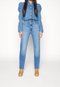 Denim button-up shirt with puffed sleeves, paired with high-waisted, light blue straight-leg jeans. Worn with tan ankle boots.