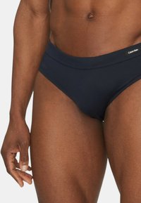 Bañadores azul marino fabricados con una tela suave; cuentan con una cinturilla ancha y una etiqueta con el logo de Calvin Klein en la parte delantera.