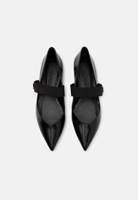 Chaussures noires à bout pointu avec une finition brillante, dotées d'une large bride élastique sur le coup de pied et d'un logo en relief sur la semelle intérieure.