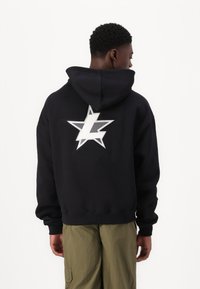 Sweatshirt preto com capuz e um grande gráfico de estrela branca e prateada nas costas. Apresenta um corte descontraído e punhos canelados.